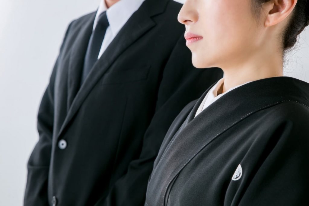 弔事の礼装である喪服着物(黒喪服)を着用した女性とブラックスーツの男性